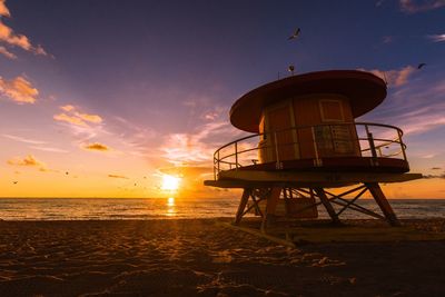 Lifeguard hut at beach against sky during sunset