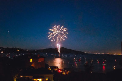 Firework display over illuminated city against sky at night