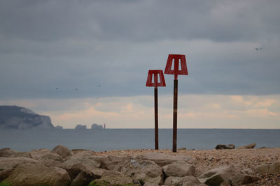 Navigation posts on beach by sea against rock formation and sky