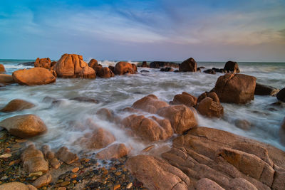 Rocks on beach against sky during sunset
