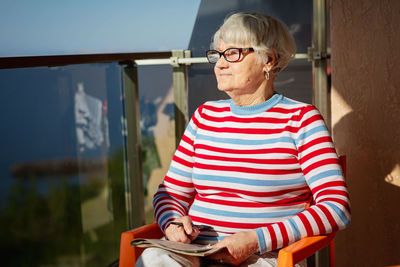 Senior woman in glasses sitting on balcony near the sea