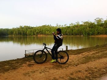 Man with bicycle on lake against sky