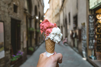 Close-up of hand holding ice cream cone against buildings