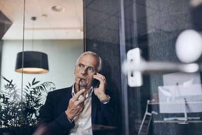 Thoughtful male manager talking on smart phone while looking away at creative office