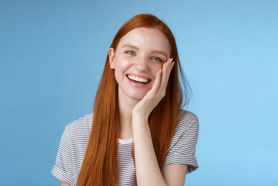 Smiling woman touching cheek against blue background