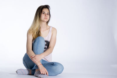 Beautiful young woman sitting against white background