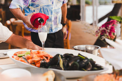 Waiter pouring sparkling champagne in a glass with food on table.