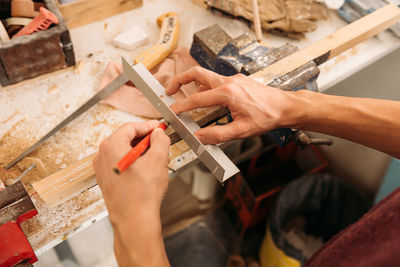 From above of crop faceless male carpenter using metal angle and wooden plank while working at workbench in bright garage