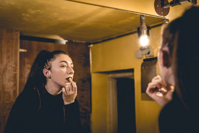 Reflection of young woman applying lipstick