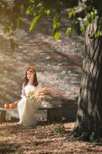 Young woman holding plants while sitting against wall