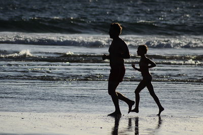 Father and son running on shore at beach