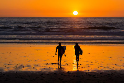 Silhouette people walking on beach during sunset