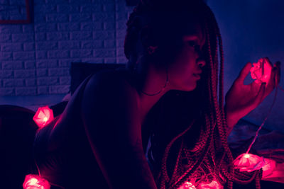 Side view of young woman holding illuminated lighting equipment lying on bed at home