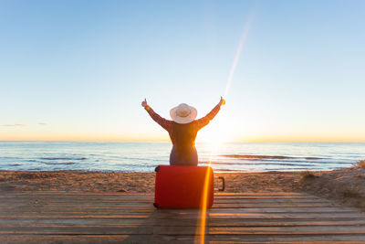 Man with arms raised on beach against clear sky