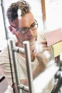 Young businessman writing adhesive notes on transparent glass in new office