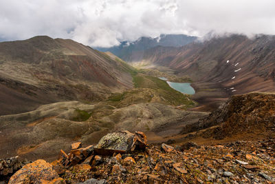 View from a rocky mountain pass into a valley with a lake. mountain ranges with clouds above them.