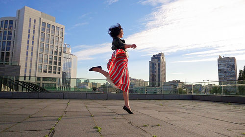 Rear view of woman jumping in city against sky