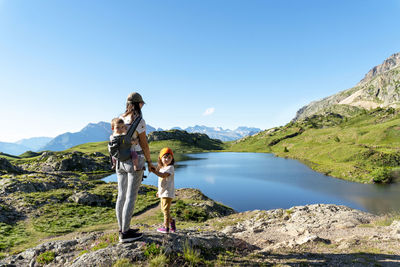 Mother with daughters standing by lakeshore on sunny day