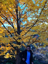 Portrait of young man standing by tree during autumn
