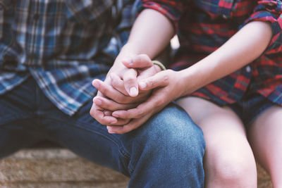 Midsection of couple holding hands while sitting outdoors