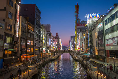 Canal amidst illuminated buildings in city during sunset