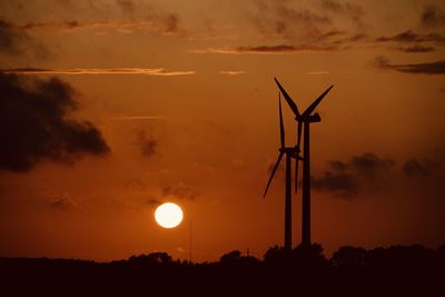 Silhouette wind turbines on field against sky during sunset