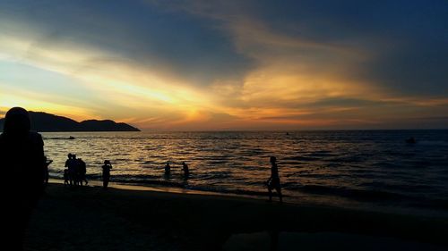 Silhouette people on beach against sky during sunset