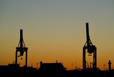 Silhouette cranes against sky during sunset