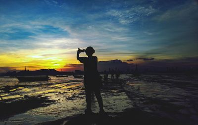 Silhouette man photographing sea against sky during sunset