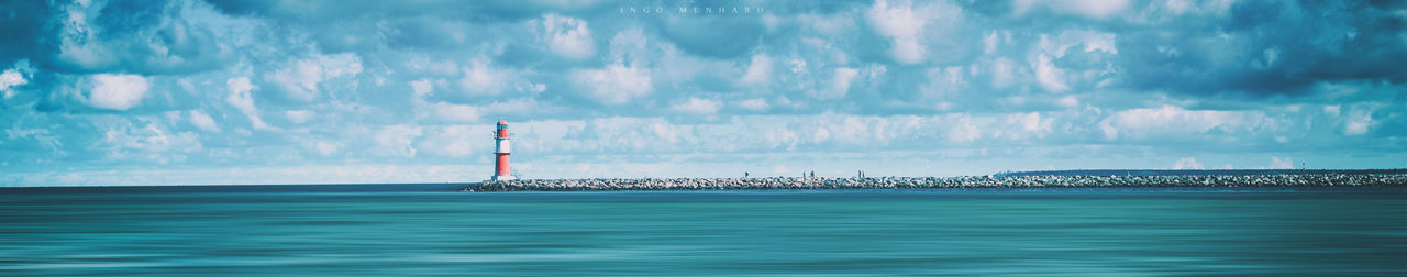 Panoramic view of lighthouse in sea against cloudy sky