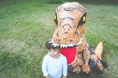 Portrait of boy standing with person wearing dinosaur costume in park