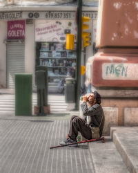 Full length of woman sitting on footpath