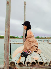 Side view of woman sitting on wood against sky