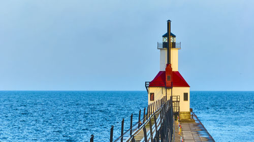 Lighthouse by sea against clear sky