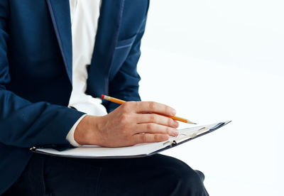 Midsection of businessman holding pencil and clipboard against white background