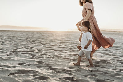 Side view of mother walking toddler twins to ocean with sun setting