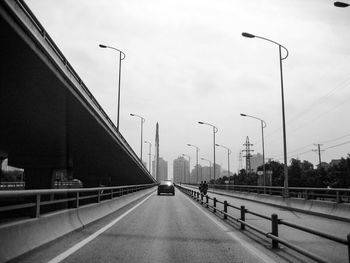 Car moving on bridge by overpass and street lights in city against clear sky