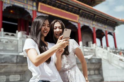 Smiling women vlogging while standing against temple