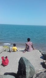 Rear view of siblings sitting on rock against sea