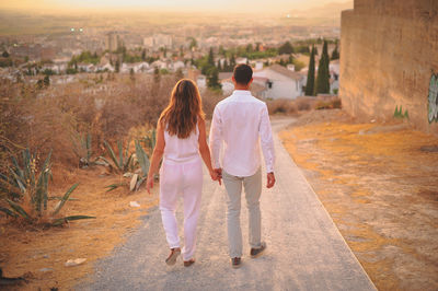 Rear view of couple walking on road during sunset