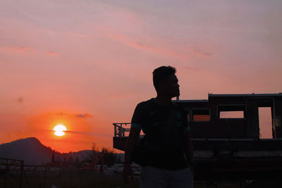 Rear view of silhouette man standing against orange sky