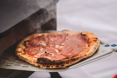 Cooking or baking hot pizza with tomato sauce, mozzarella and salami meat with a shovel