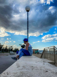 Rear view of man sitting on pier against sky