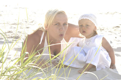 Portrait of mother and daughter resting at beach on sunny day