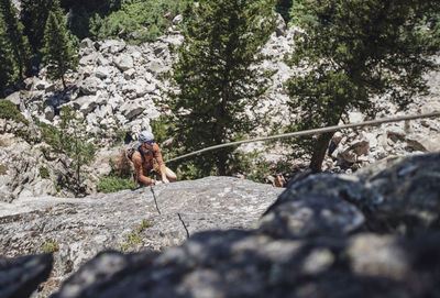A young man wearing helmet hangs from rope while rock climbing