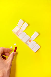 Cropped hand of person holding toy blocks against yellow background