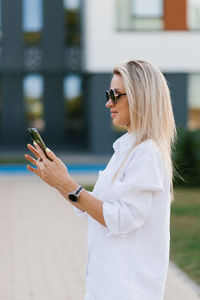 Pretty young blonde of caucasian nationality looks at the smartphone screen while walking 