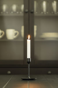 White burning candle in holder over black dining table - vertical