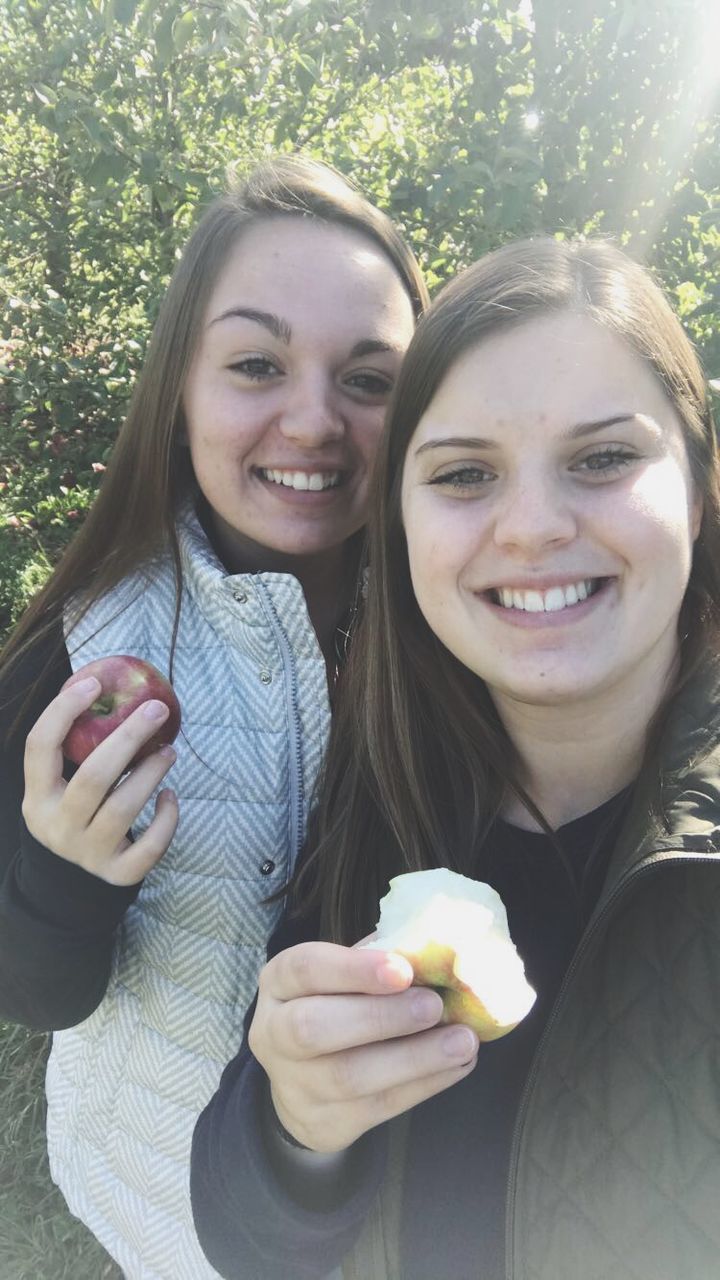 looking at camera, smiling, portrait, real people, young women, holding, young adult, fruit, happiness, food and drink, casual clothing, leisure activity, two people, front view, togetherness, lifestyles, day, food, bonding, friendship, outdoors, selfie, eating, healthy eating, tree, close-up