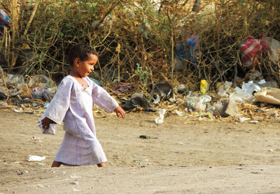 Side view of girl walking on dirt road against plants